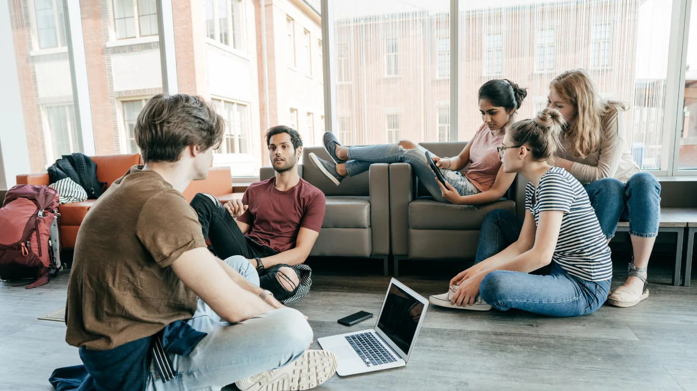 Groupe d'étudiants assis en cercle dans un hall universitaire, discutant de la répartition des tâches